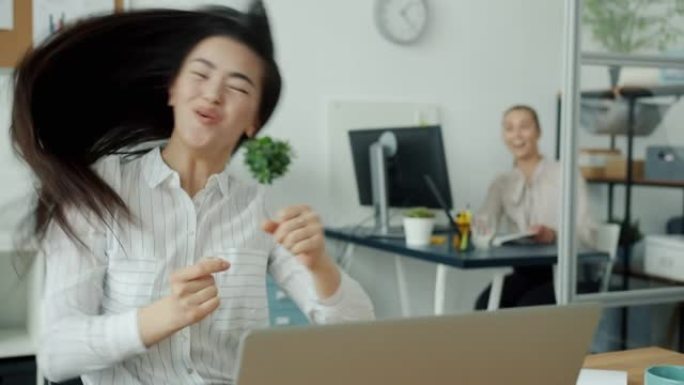 快乐的亚洲女人用笔记本电脑工作，然后享受成功跳舞的乐趣