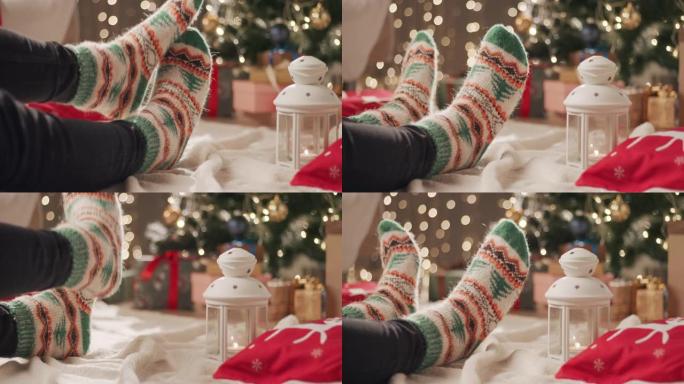 一个穿着圣诞节图案的袜子的男人坐在圣诞树附近的毯子上，用另一条腿刮擦