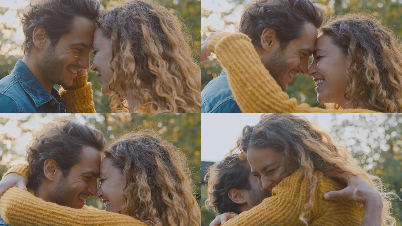幸福的情侣微笑着，男人在秋天的公园里拥抱着女人