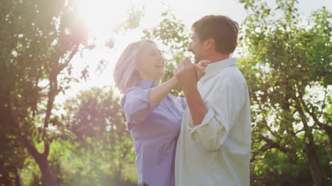 可爱的快乐成熟夫妇的真实特写镜头是享受时间在一起，并在绿色自然的背景下跳舞庆祝他们永恒的爱。