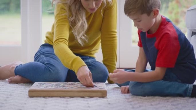 母子俩在家一起在休息室地板上做拼图游戏