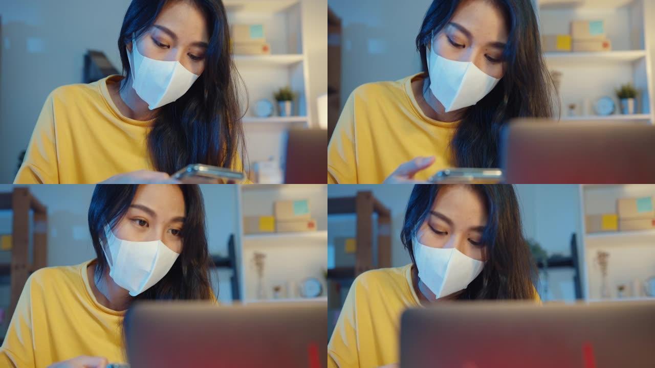 年轻的亚洲女商人戴着口罩检查智能手机上的采购订单，晚上在家庭办公室的电脑中库存。