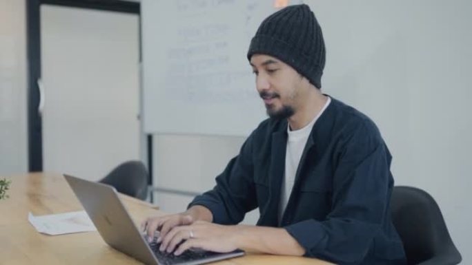时髦的亚洲男人坐着用笔记本电脑学习。