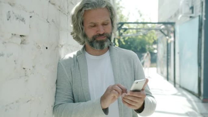 成熟的大胡子家伙在街上用智能手机发短信独自一人触摸屏幕