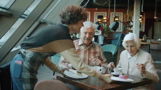 老年夫妇使用智能手机聊天，而女服务员在咖啡馆里带甜点