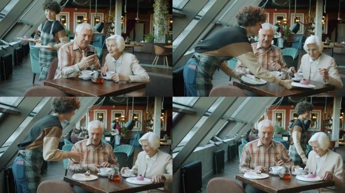 老年夫妇使用智能手机聊天，而女服务员在咖啡馆里带甜点