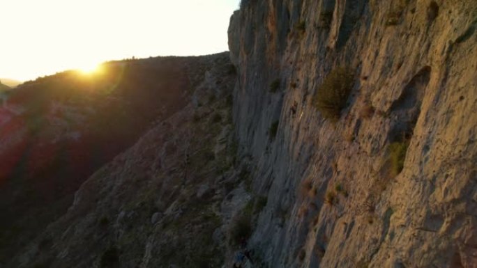空中: 女性登山者在背景中带着金色的太阳耀斑爬上墙