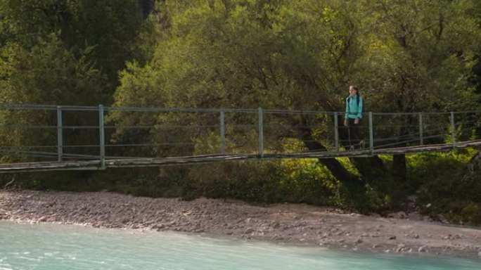 一名年轻女游客在山河上的一座木桥上徒步旅行的移动镜头