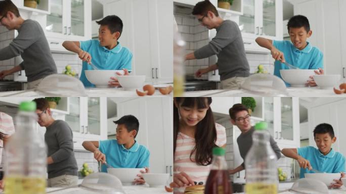 快乐的亚洲父亲在厨房里与大笑的儿子和女儿一起做早餐