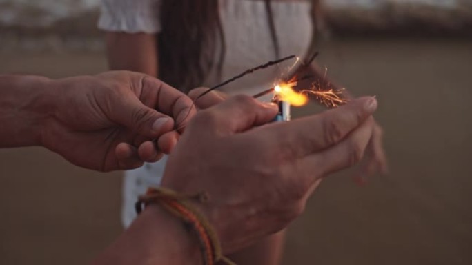 SLO MO夫妇在海滩上晚上用打火机点燃烟火，特写