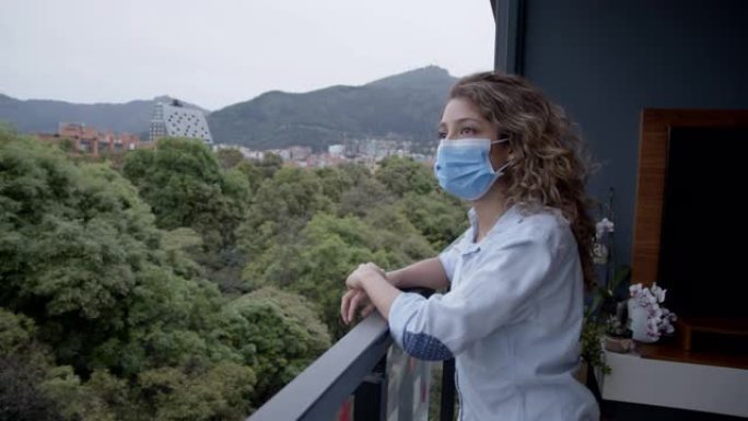 检疫的悲伤女人戴着口罩透过窗户看着风景
