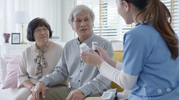 年轻的护理人员穿着磨砂膏制服，向老年亚洲夫妇男女展示药瓶，上门护理服务。具有辅助生活药物监测概念的亚