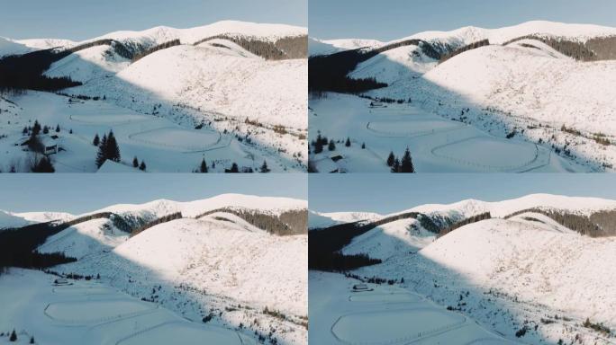 无人机飞越两个被雪覆盖的溜冰场，朝着美丽的寒冷阳光明媚的冬季景观山脉飞行。
