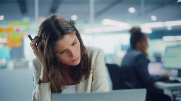 年轻严肃的女经理在现代办公室使用电脑。过度劳累的员工处理艰苦的工作任务。压力很大的美女精疲力尽，想出