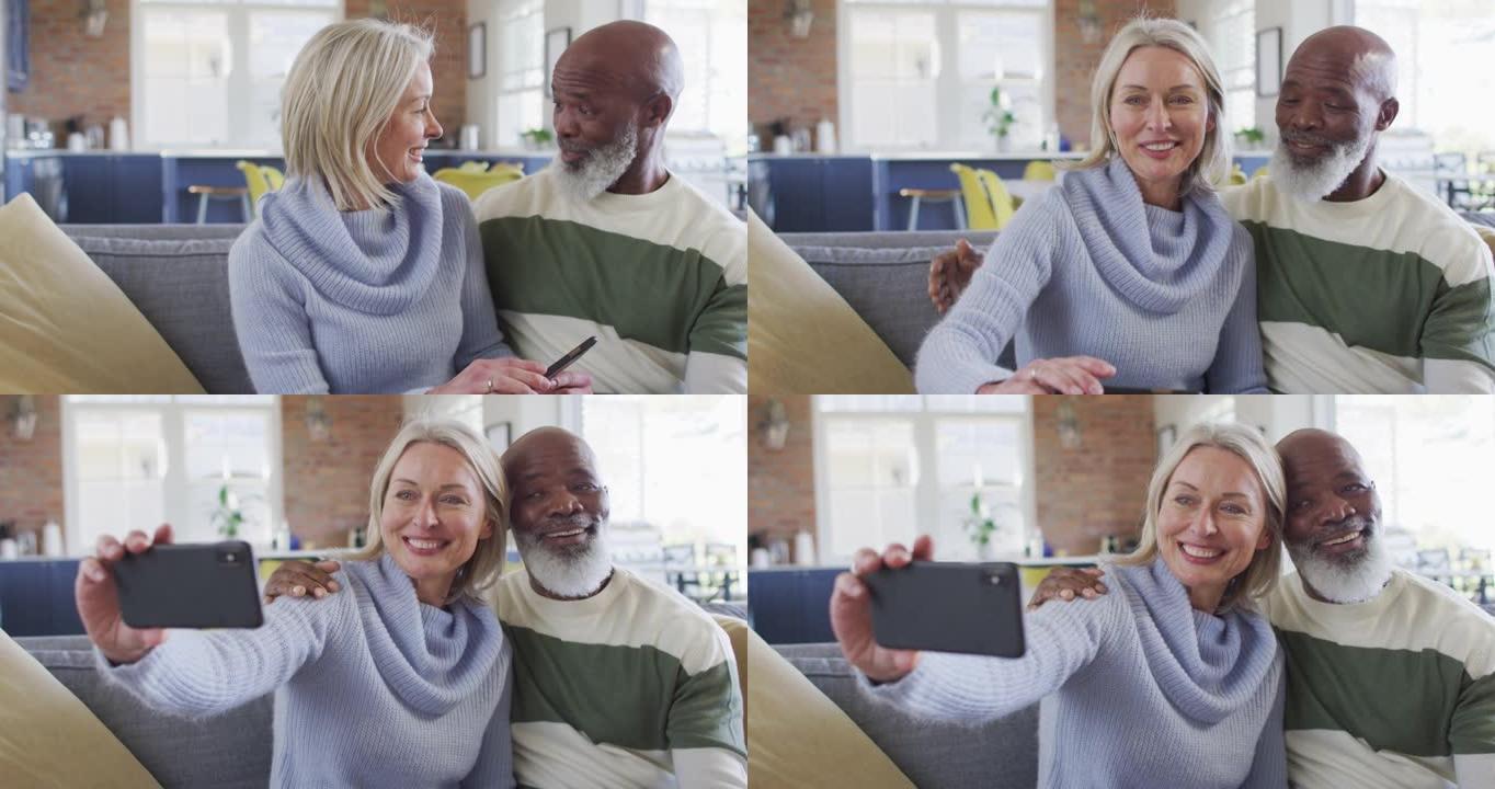 快乐的老年多样化夫妇坐在沙发上，使用智能手机，进行视频通话