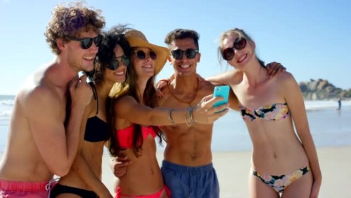 4k视频片段，一群不同的朋友一起站在海滩上并在手机上自拍