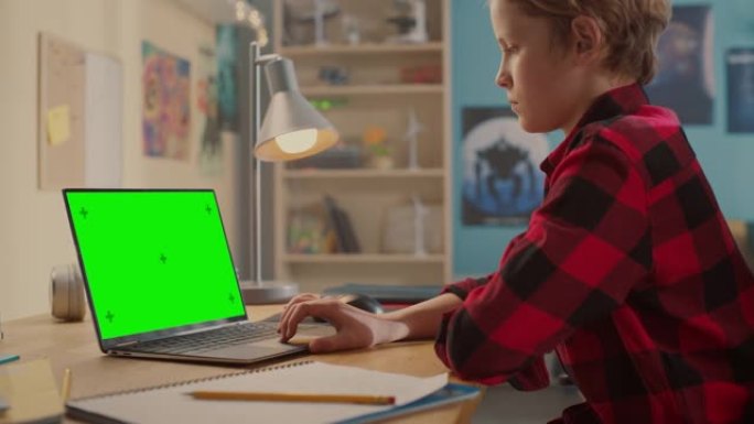 聪明的小男孩在带有绿色色度键屏幕显示模型的笔记本电脑上研究作业。青少年浏览教育研究，在社交媒体上聊天