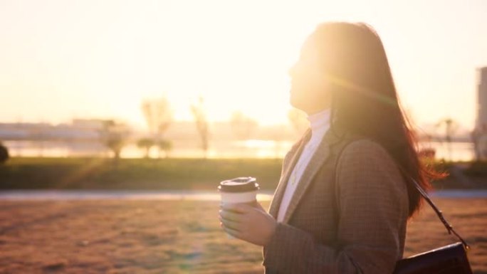 年轻妇女手持纸咖啡杯在城市早晨行走