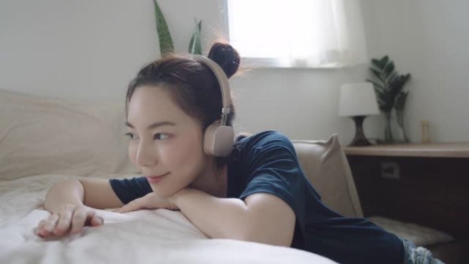 快乐的亚洲女人在卧室里用耳机听音乐。