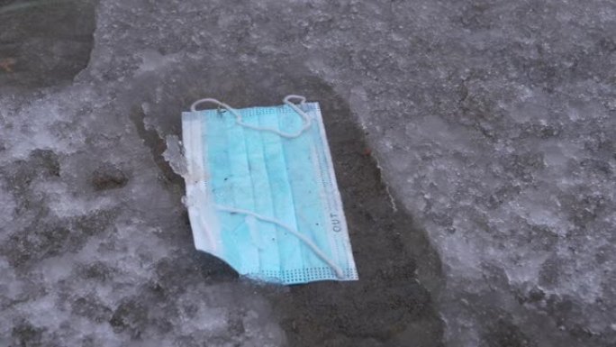 特写: 防护口罩被扔在覆盖着融化的雪泥的街道上。