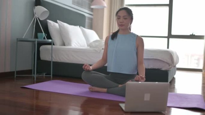 亚洲中国女性在家庭卧室练习瑜伽，使用笔记本电脑进行在线课程