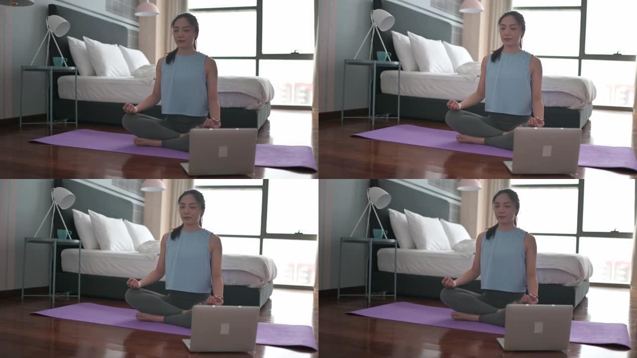 亚洲中国女性在家庭卧室练习瑜伽，使用笔记本电脑进行在线课程