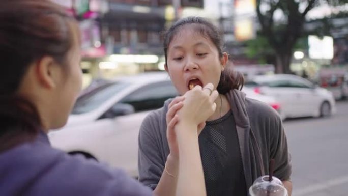 年轻女子给朋友喂食物。泰国街头美食。