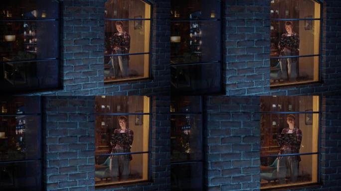 富有创造力的职业女性在家在时尚的客厅工作。女性站在窗前，浏览互联网，查看社交媒体和公司邮箱。通过窗口