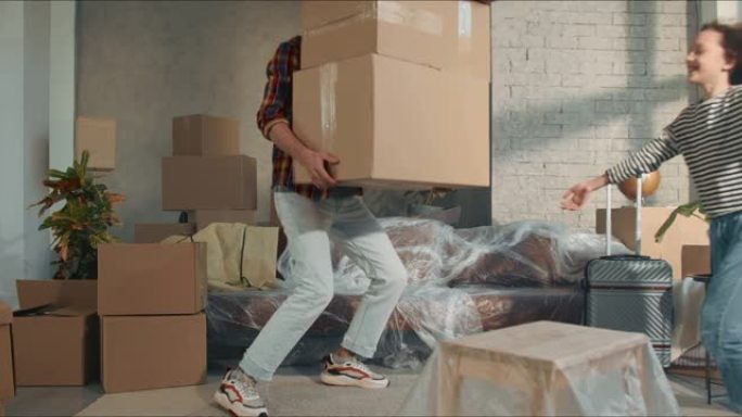 一名男子背着大箱子，在新的宽敞轻便的公寓里移动，孩子们跑来跑去，摔倒在沙发上。