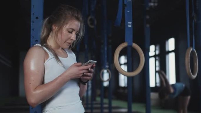 美丽疲惫的金发运动员女人在现代健身房激烈锻炼后，使用智能手机跟踪体育活动。