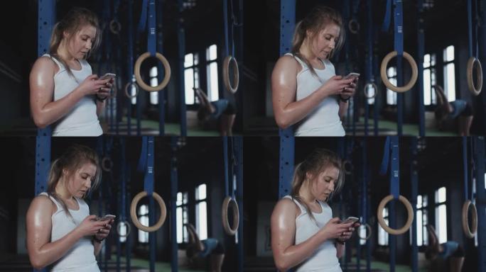 美丽疲惫的金发运动员女人在现代健身房激烈锻炼后，使用智能手机跟踪体育活动。