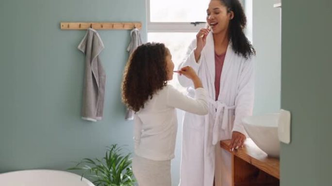 家庭住宅，浴室和母亲和女儿一起刷牙，学习良好的卫生习惯和牙齿习惯，以促进健康。黑人妇女和女童早上一起