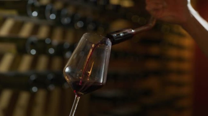 近距离拍摄酿酒师或侍酒师正在将红酒倒入透明玻璃杯中，以品尝风味并检查酒窖中的质量。