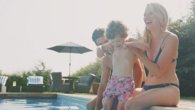 带着小儿子坐在游泳池边的家庭在户外游泳池度过暑假