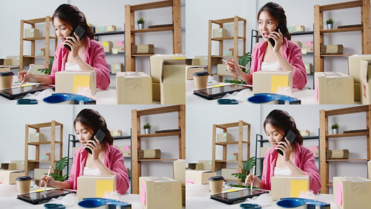 年轻的亚洲女商人使用手机电话接收采购订单并检查库存产品，在家庭办公室工作。