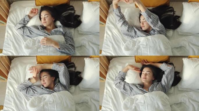 可爱的年轻亚洲女人睡觉然后醒来并在舒适的床上伸展手臂的俯视图