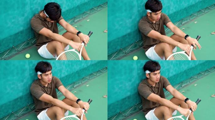 失望的男子网球运动员坐在球场上。