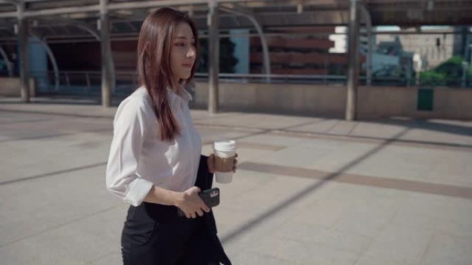 自信的年轻女商人在穿越城市时喝咖啡