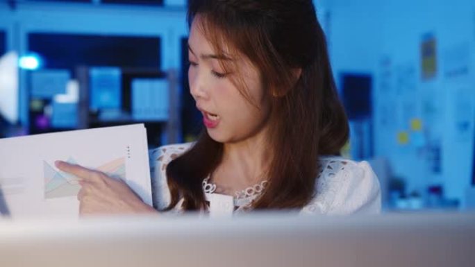 亚洲女商人在预防病毒的新常态下保持社交距离在办公室晚上工作时向同事介绍有关视频通话计划的笔记本电脑演