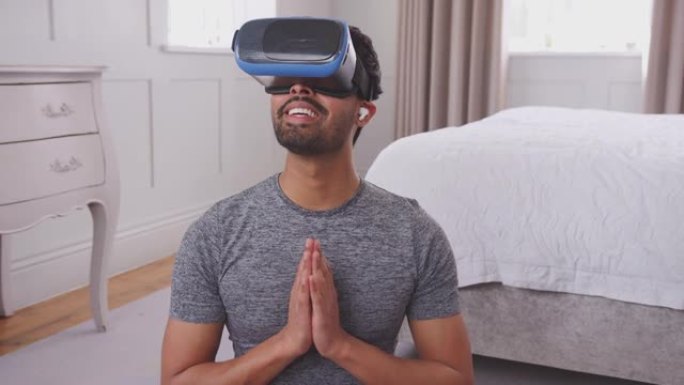 男人戴着虚拟现实耳机和耳机坐在家里卧室的瑜伽垫上