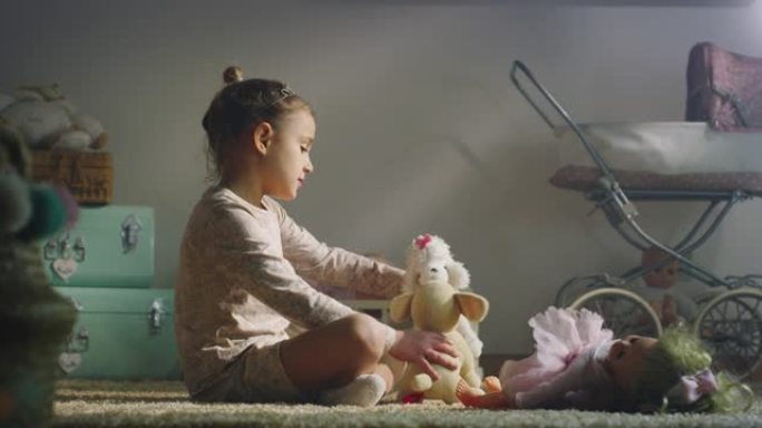 穿着睡衣的小女孩的电影镜头正坐在舒适的地毯上，在托儿所醒来时，和她的泰迪熊一起玩很开心。爱情、童年、