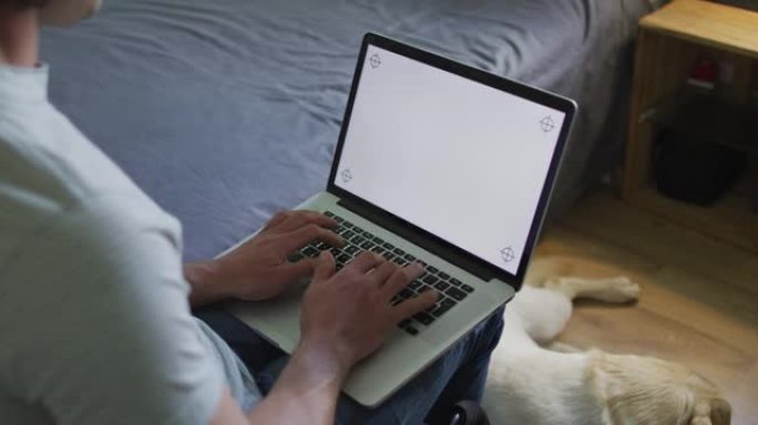 白人男子在卧室里和宠物狗一起使用笔记本电脑