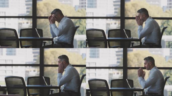 紧张或疲倦的成熟商人坐在会议室桌上的笔记本电脑上工作