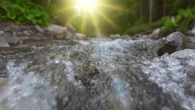 森林里的山河。相机沿着水和石头的表面移动，在背景中晒太阳和绿色植物。慢动作UHD镜头