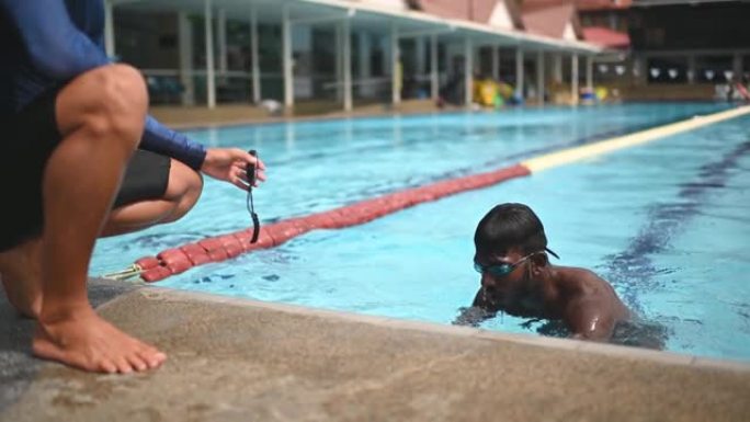 亚洲中国私人教练在运动训练期间在泳池边向学生展示秒表时间记录