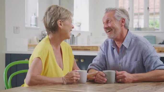 亲吻退休夫妇坐在家里的桌子旁一起喝早间咖啡