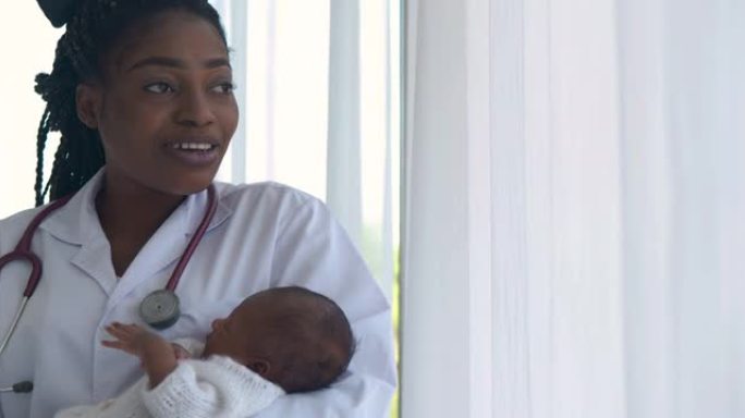 非洲民族儿科医生的女医生，新生儿在她的怀抱中休息，同时透过医院的窗户看。怀孕/出生概念。
