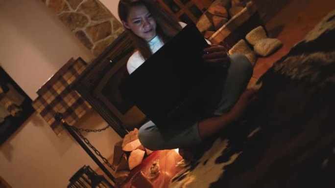 女人坐在家里壁炉旁的地板上使用笔记本电脑