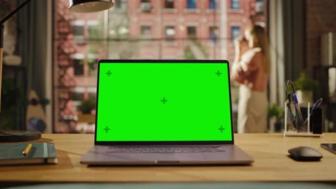 笔记本电脑显示器，在客厅的桌子上显示绿屏模拟。家里或创意阁楼办公室的色度钥匙监视器，女性从杯子里喝酒