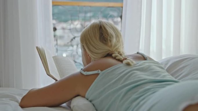 SLO MO女人在海边的酒店房间的床上看书